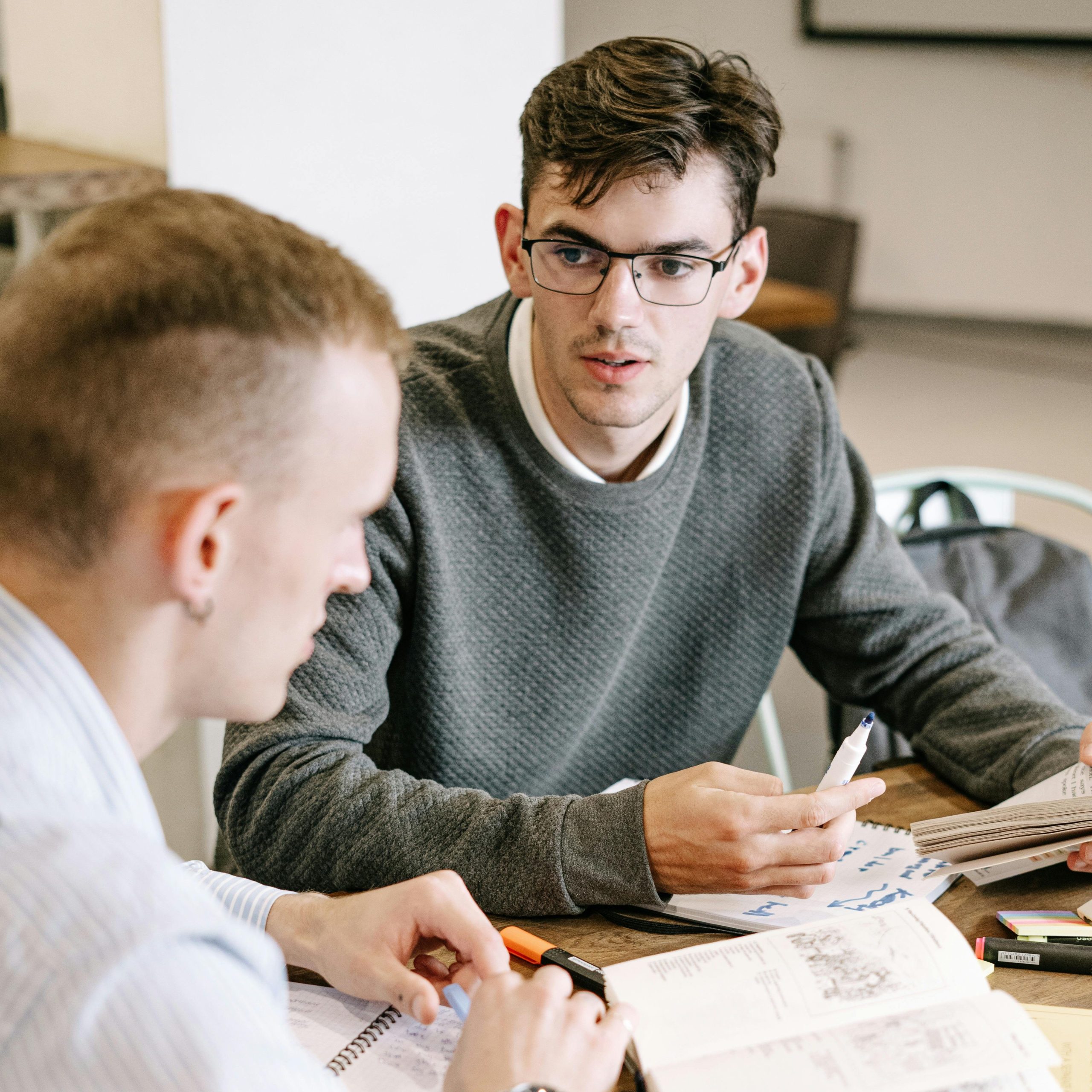 pexels-photo-5676678-5676678 Two young men studying together at a table with books and notes.